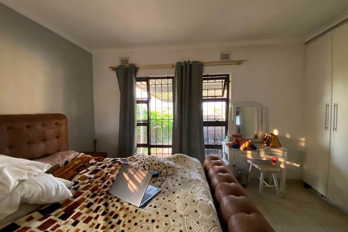 A bedroom featuring built-in cupboards, tiled flooring, and security bars on the windows, providing a functional and secure living space.