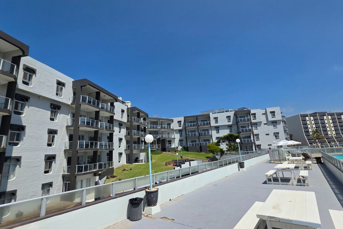 Exterior view of a multi-story apartment complex featuring private balconies, a communal terrace area, and landscaped grounds.