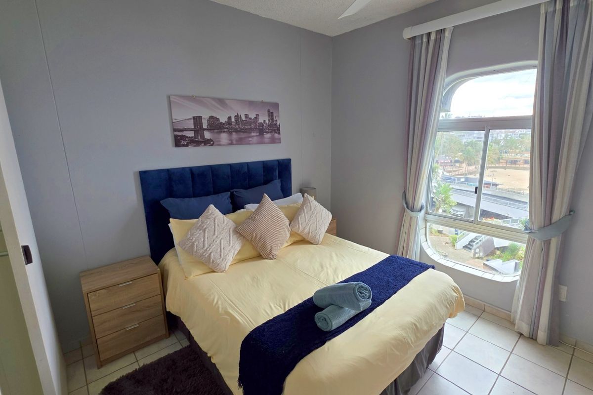 A bedroom featuring tiled flooring, a large arched window with exterior views, and neutral wall finishes.