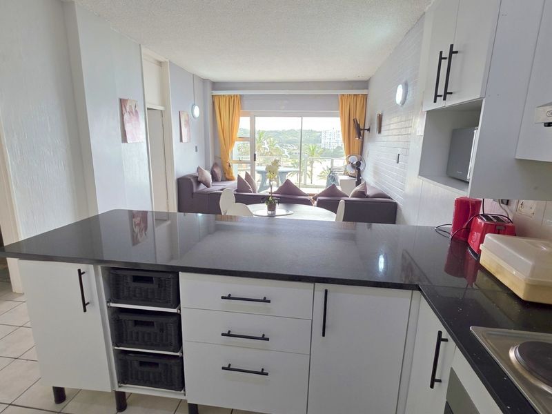 Open plan kitchen and living area featuring modern white cabinetry, dark stone countertops, and direct access to a balcony with scenic views.
