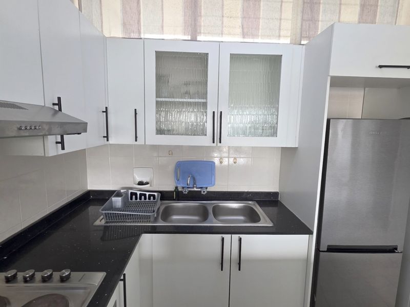 A functional kitchen featuring white cabinetry, dark stone countertops, a double stainless steel sink, and a built-in extractor fan.