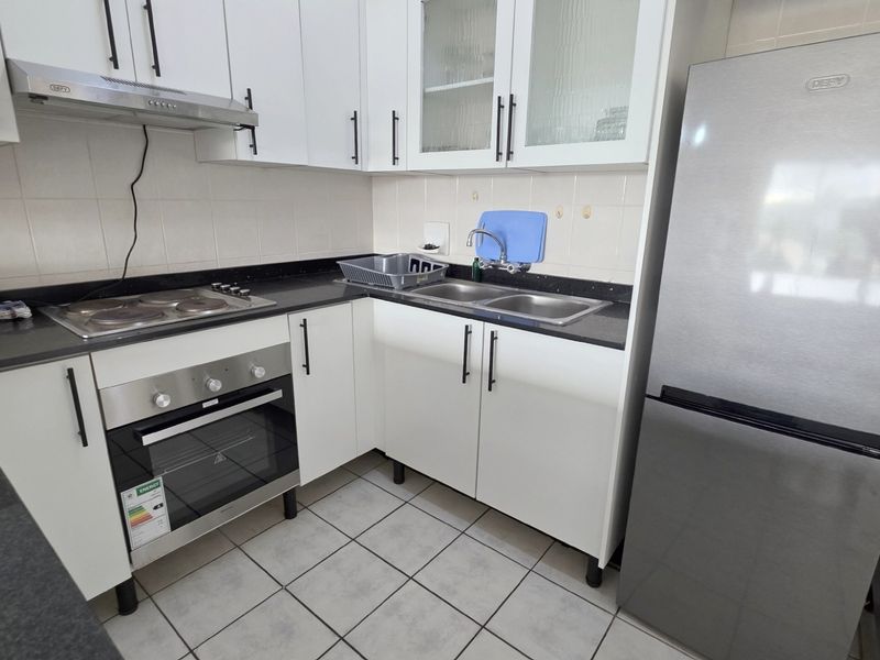 Compact kitchen featuring white cabinetry, dark granite countertops, built-in oven, electric hob, extractor fan, and double stainless steel sink.