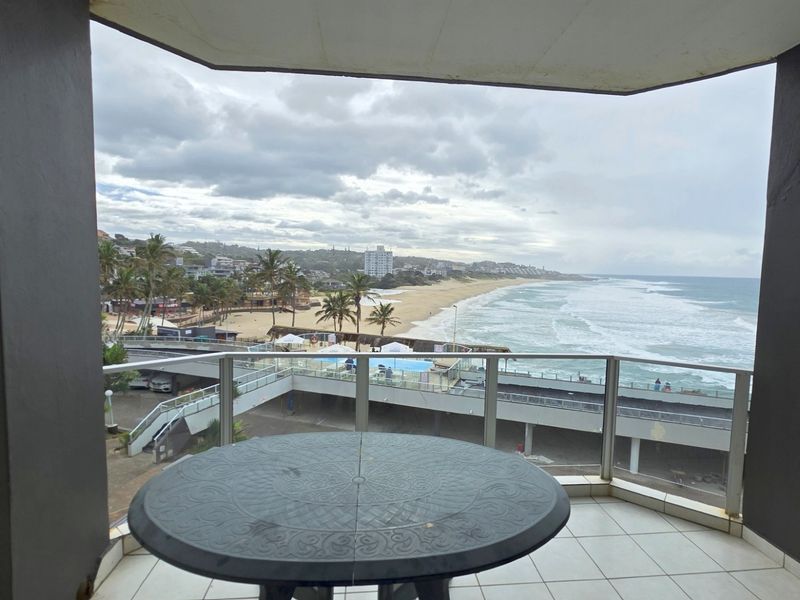 Covered balcony featuring tiled flooring and a glass balustrade, offering expansive panoramic views of the coastline and ocean.