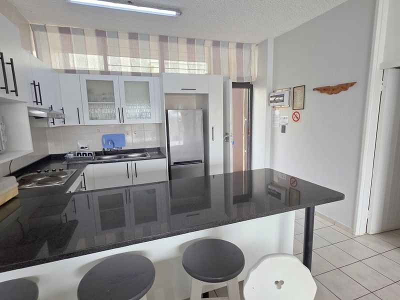 A functional kitchen featuring white cabinetry, dark granite countertops, a breakfast bar, and tiled flooring, providing a practical layout for daily use.