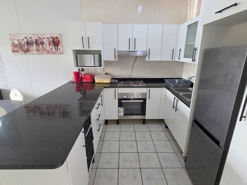 Compact kitchen featuring white cabinetry, dark granite countertops, built-in oven, hob, extractor fan, and tiled flooring with an integrated breakfast bar.
