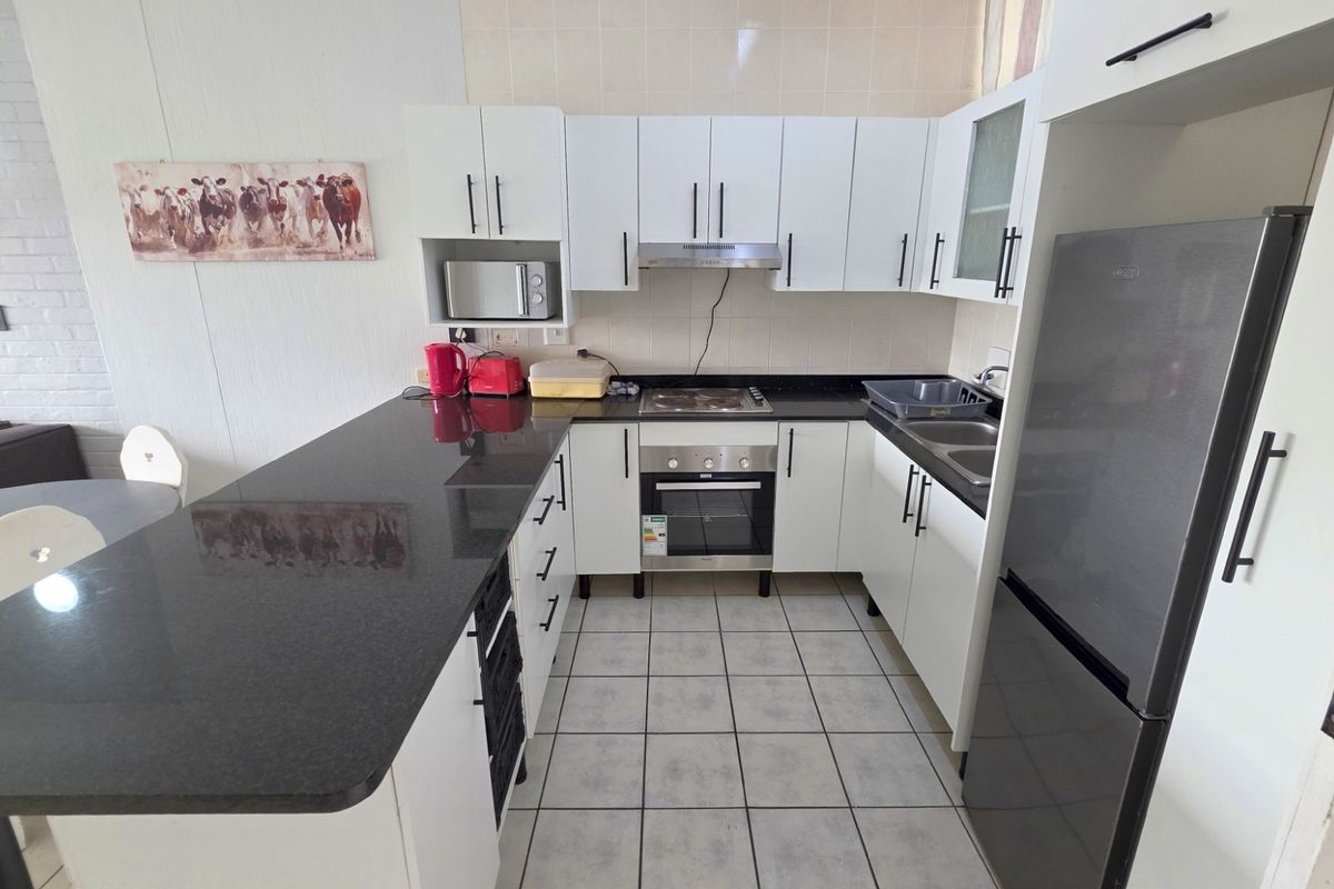 Compact kitchen featuring white cabinetry, dark granite countertops, built-in oven, hob, extractor fan, and tiled flooring with an integrated breakfast bar.