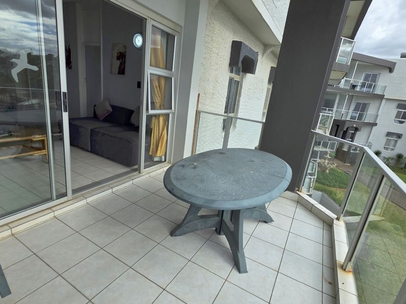 A covered balcony featuring tiled flooring and glass balustrades, providing an outdoor space accessible through sliding doors from the interior living area.