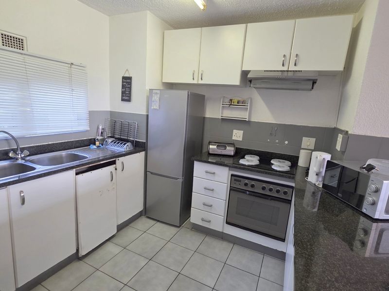 A functional kitchen featuring white cabinetry, dark granite countertops, a built-in oven with hob, and a double stainless steel sink.