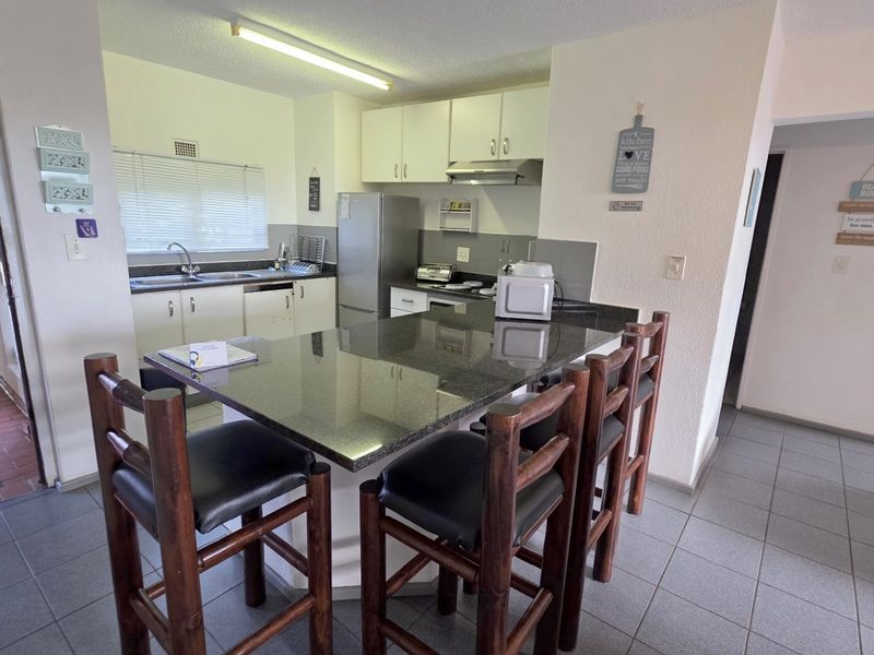 Open-plan kitchen featuring a granite breakfast bar, built-in cabinetry, stainless steel sink, and tiled flooring, seamlessly connecting to the living area.