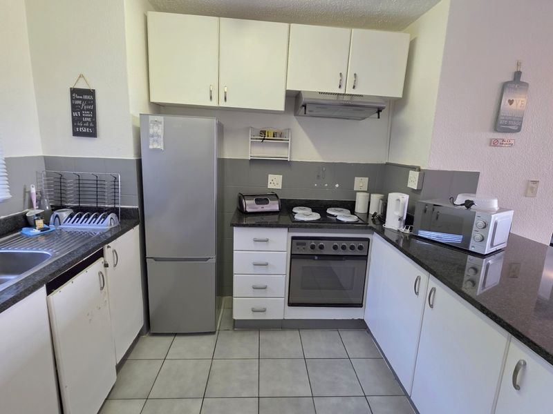 A functional kitchen featuring dark granite countertops, white cabinetry, a built-in oven with hob, extractor fan, and a double stainless steel sink.