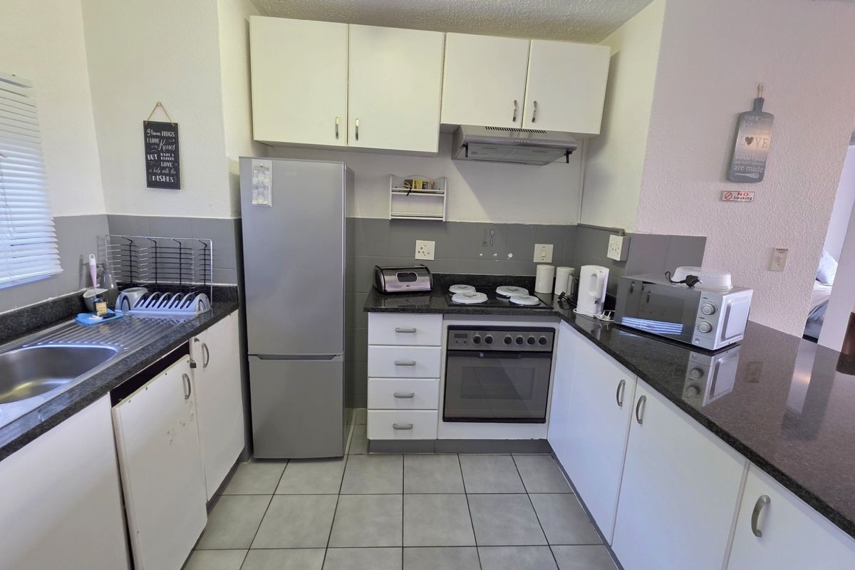 A functional kitchen featuring dark granite countertops, white cabinetry, a built-in oven with hob, extractor fan, and a double stainless steel sink.