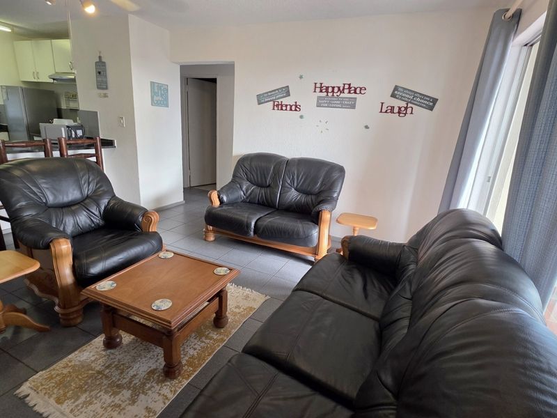 Open plan living area featuring tiled flooring, integrated kitchen with breakfast bar, and sliding door access to the balcony.