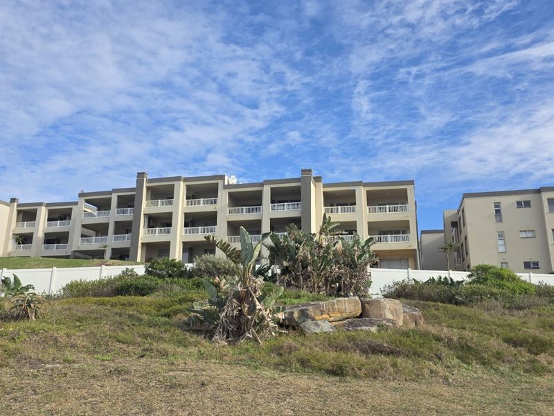 Exterior view of a multi-story apartment complex featuring private balconies and a landscaped foreground.
