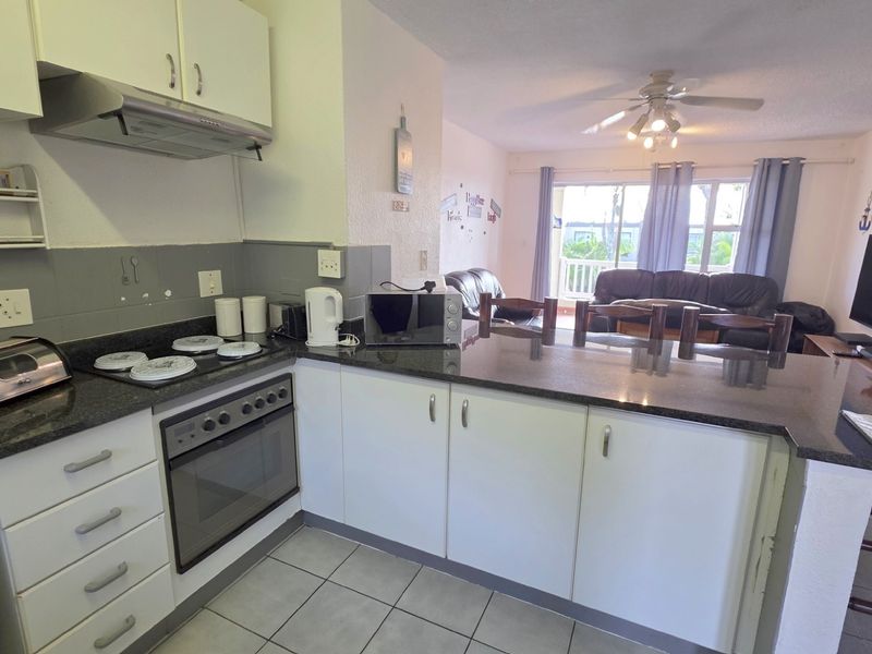 Open-plan kitchen featuring granite countertops, built-in oven, and hob, flowing into a living area with access to a balcony.
