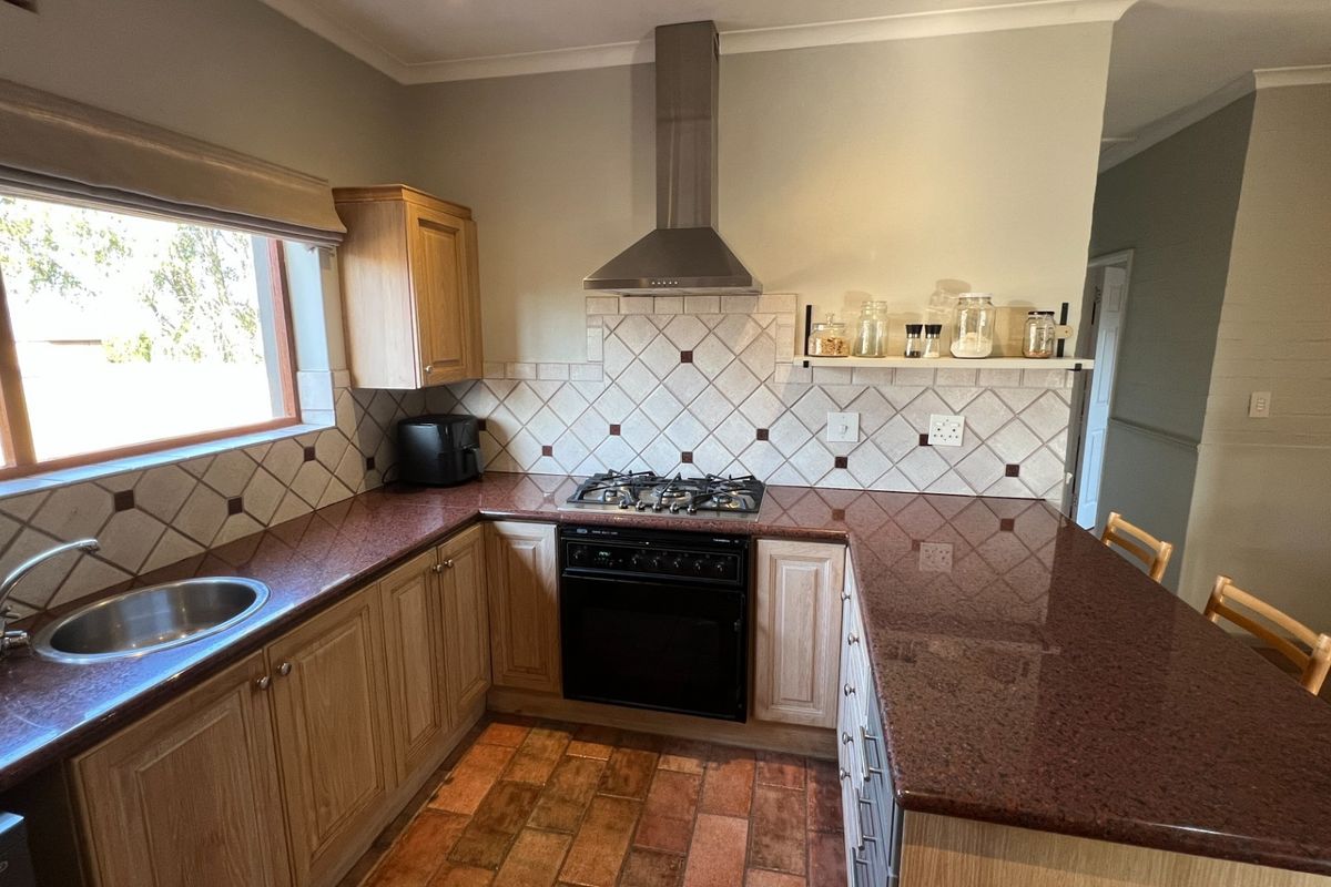 A functional kitchen featuring granite countertops, a built-in gas hob, an oven with an extractor fan, and tiled flooring.