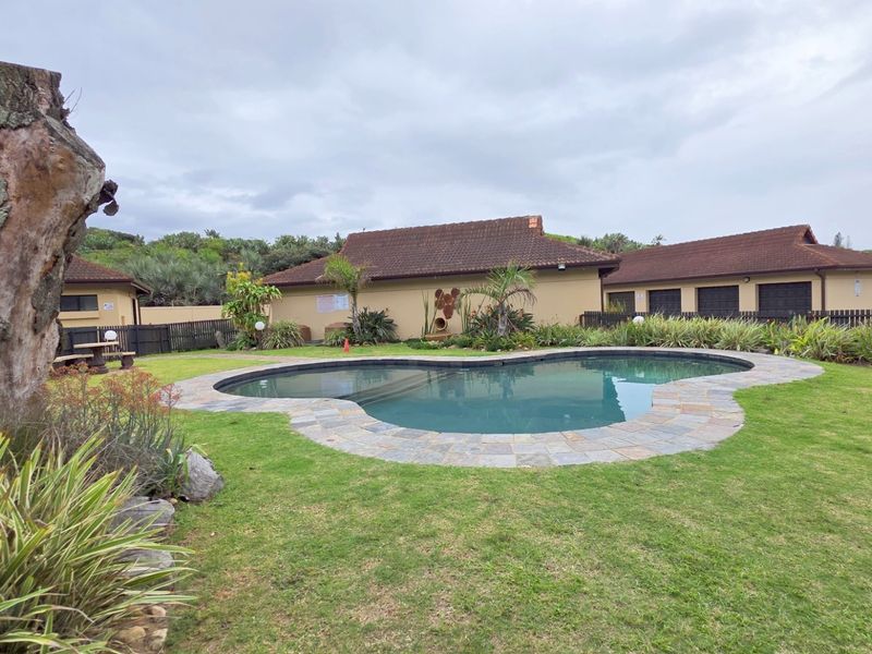A communal outdoor area featuring a kidney-shaped swimming pool with stone paving, surrounded by a landscaped garden and residential building units.