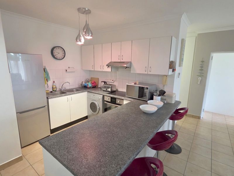 A functional kitchen featuring white cabinetry, a granite-look breakfast bar, built-in oven, extractor fan, and tiled flooring in an open-plan layout.