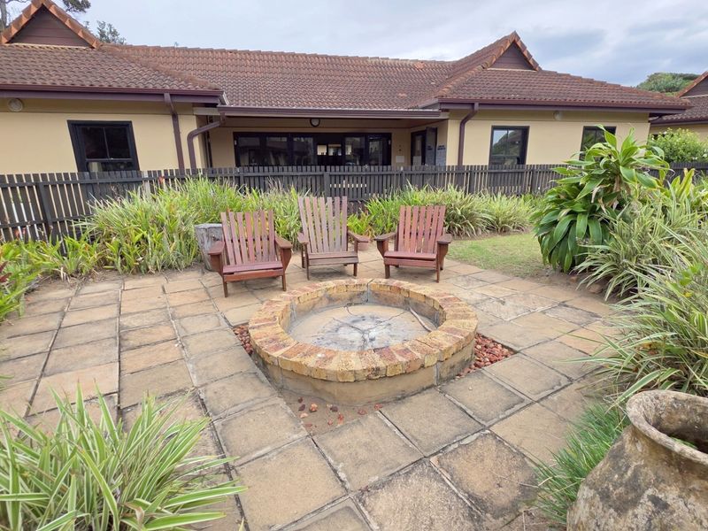 Outdoor patio area featuring a circular brick fire pit, paved flooring, and established garden landscaping set against the rear building elevation.