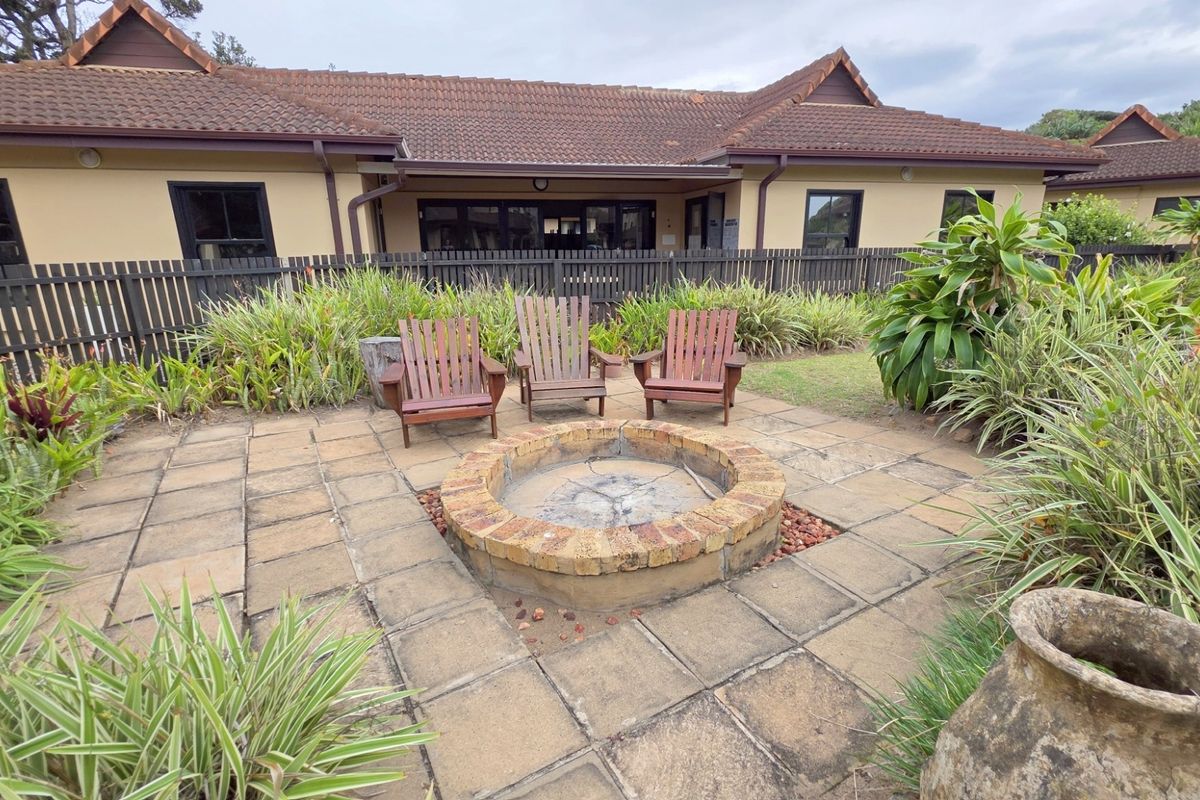 Outdoor patio area featuring a circular brick fire pit, paved flooring, and established garden landscaping set against the rear building elevation.