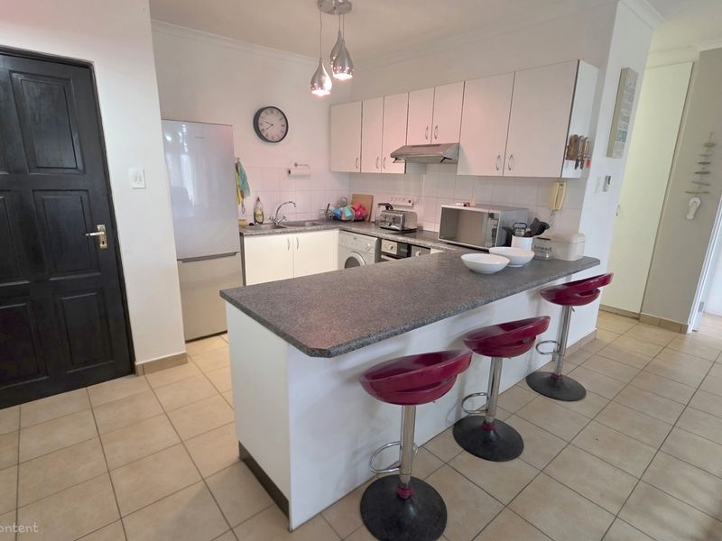 Open-plan kitchen featuring a breakfast bar, built-in cabinetry, extractor fan, and tiled flooring, seamlessly connecting to the living area.