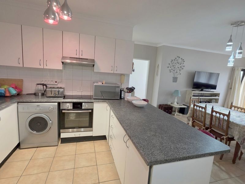 Open-plan kitchen and dining area featuring white cabinetry, granite-look countertops, integrated oven, hob, extractor fan, and tiled flooring throughout.
