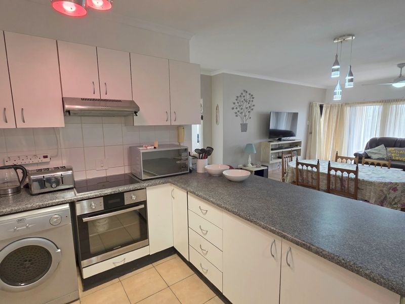 Open-plan kitchen and living area featuring built-in cabinetry, integrated oven, hob, extractor fan, and tiled flooring throughout the combined space.