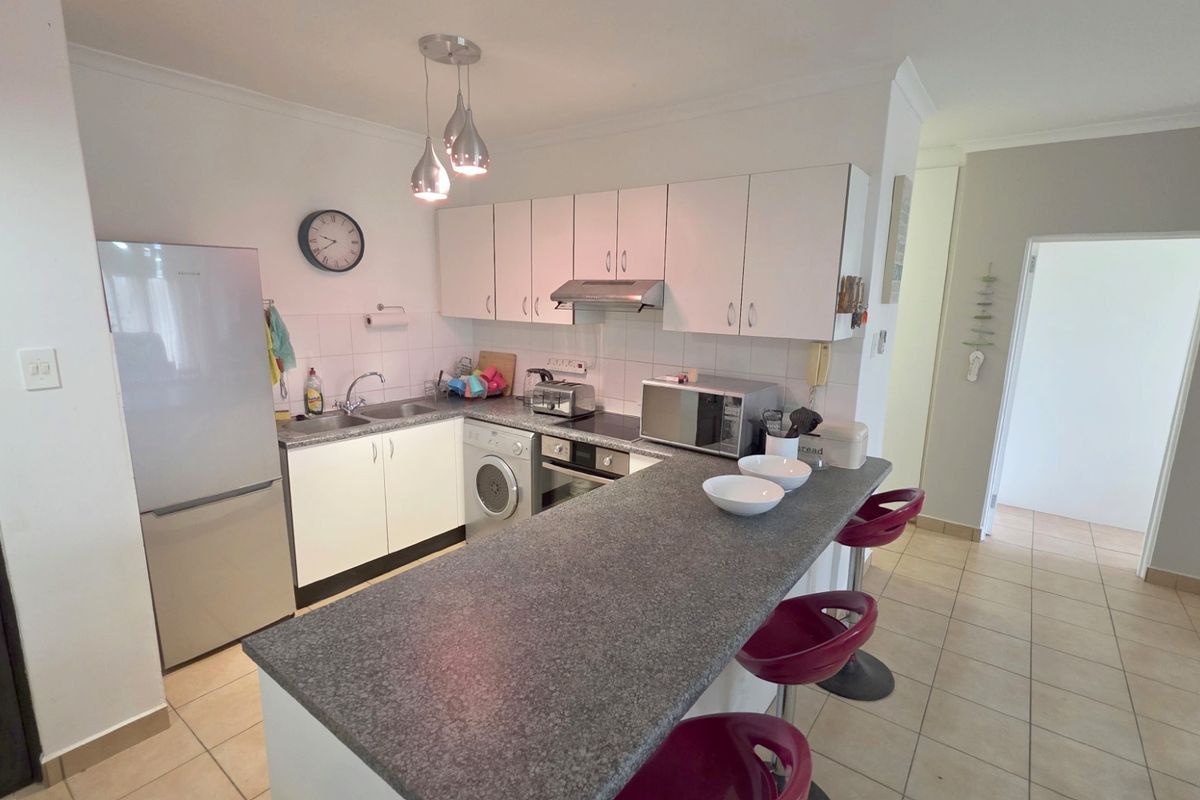 A functional kitchen featuring white cabinetry, a granite-look breakfast bar, built-in oven, extractor fan, and tiled flooring in an open-plan layout.