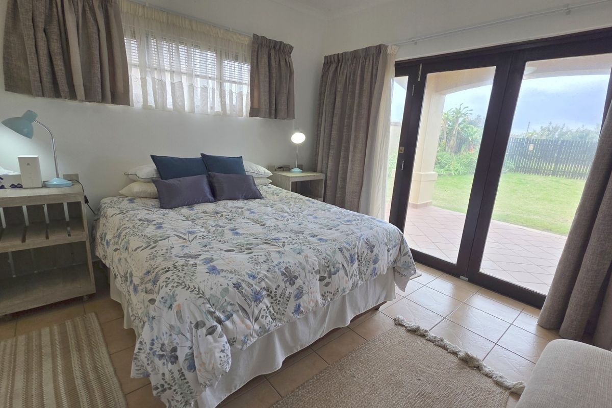 A bedroom featuring tiled flooring and sliding glass doors that provide direct access to a covered patio and garden area.