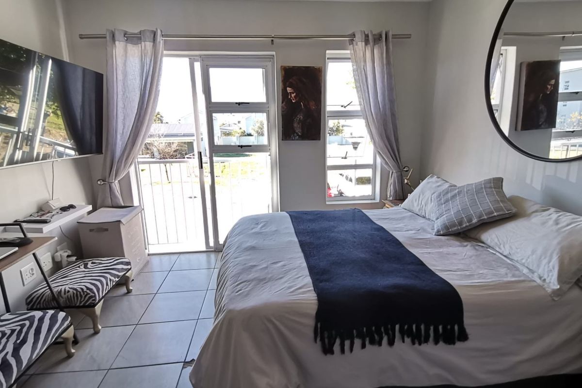 A bedroom featuring tiled flooring, large windows, and a sliding glass door providing access to a balcony.