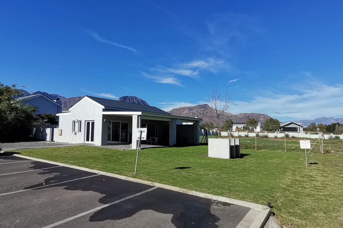 A view of the rear exterior of the apartment, featuring a covered patio, landscaped lawn, and a built-in outdoor braai area.