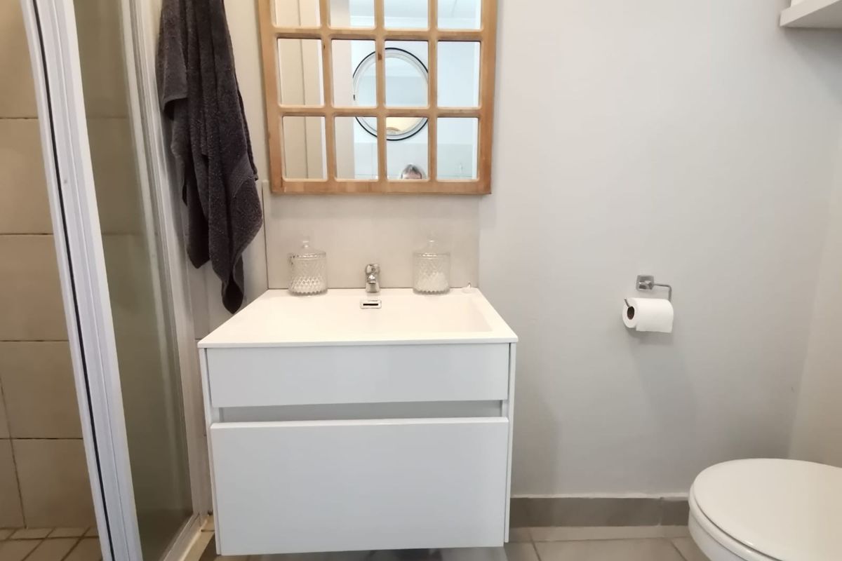 A clean, modern bathroom featuring a wall-mounted vanity with a basin, a shower enclosure, and a toilet.