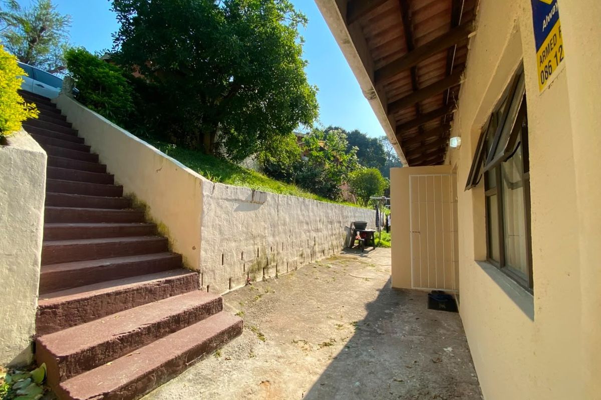 Exterior side pathway featuring concrete stairs leading to an elevated garden area, adjacent to the main building structure with a security sign.
