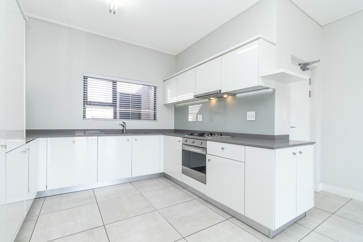 Modern kitchen featuring white high-gloss cabinetry, grey stone countertops, integrated stainless steel oven, gas hob, and extractor fan with tiled flooring.