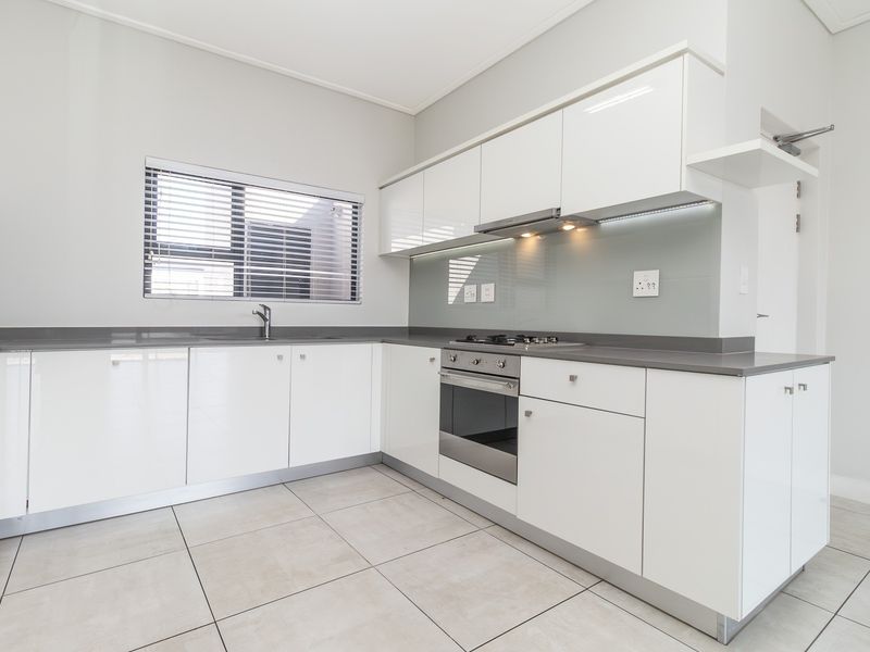 Modern kitchen featuring white high-gloss cabinetry, grey stone countertops, a glass splashback, and integrated stainless steel oven and gas hob.
