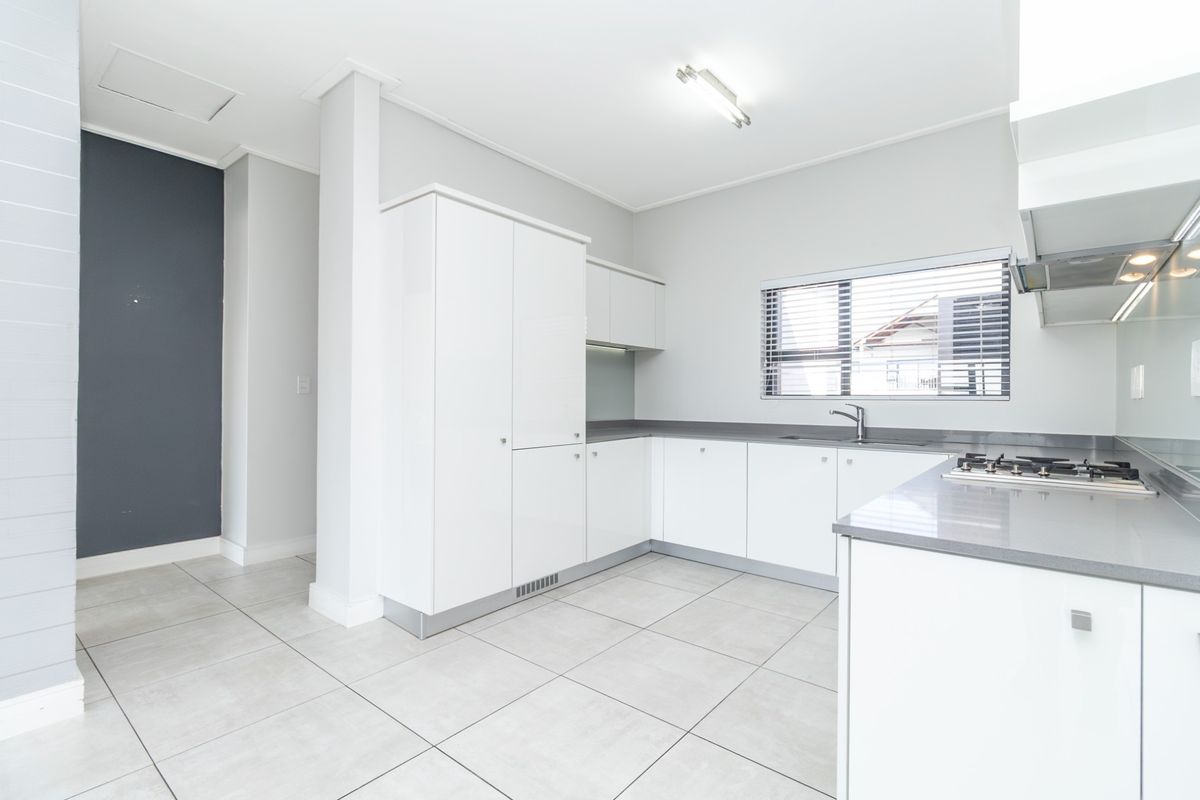 Modern kitchen featuring white cabinetry, stone countertops, a built-in gas hob, and an integrated extractor fan with tiled flooring.