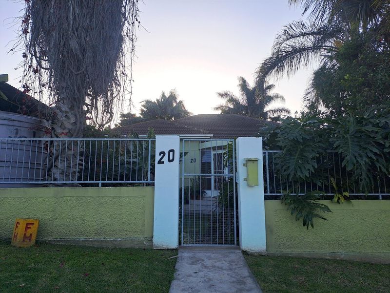 Front view of the property featuring a gated entrance, perimeter wall, and concrete walkway leading to the main house entrance.