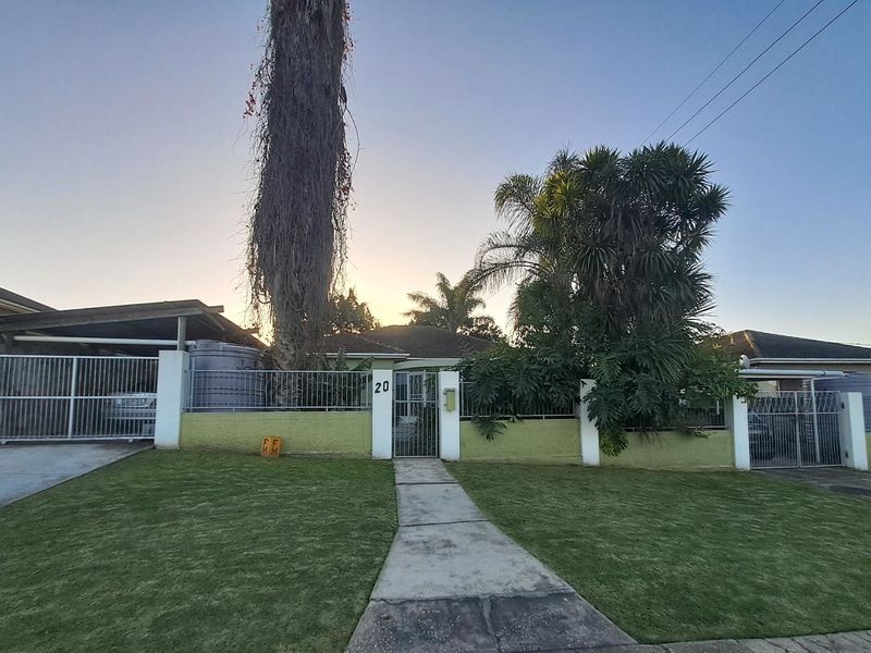 Front view of the property featuring a gated entrance, concrete driveway, carport, and established garden area with perimeter walling.