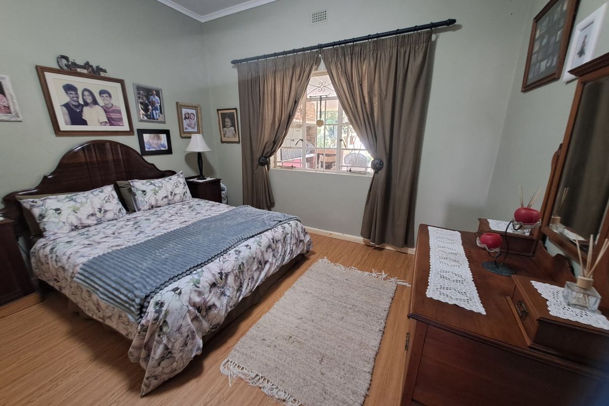 A well-maintained bedroom featuring laminate flooring, a window with security bars, and neutral wall tones.