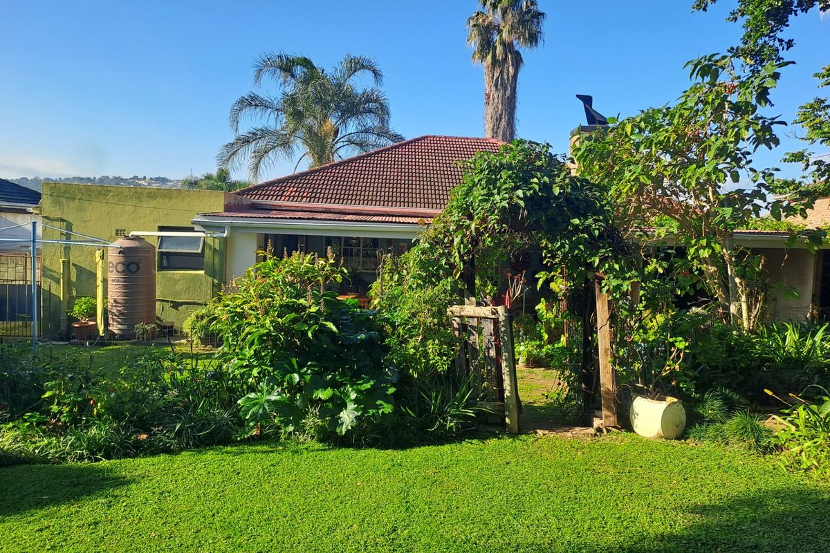 A view of the rear garden featuring a lawn, established greenery, a wooden garden arch, and a water storage tank against the house exterior.