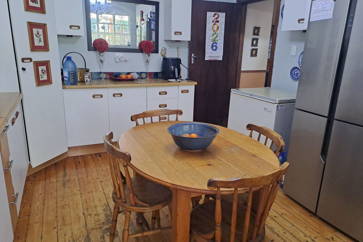A functional kitchen featuring white cabinetry, timber flooring, and a dedicated dining area, providing a practical space for daily meals and food preparation.