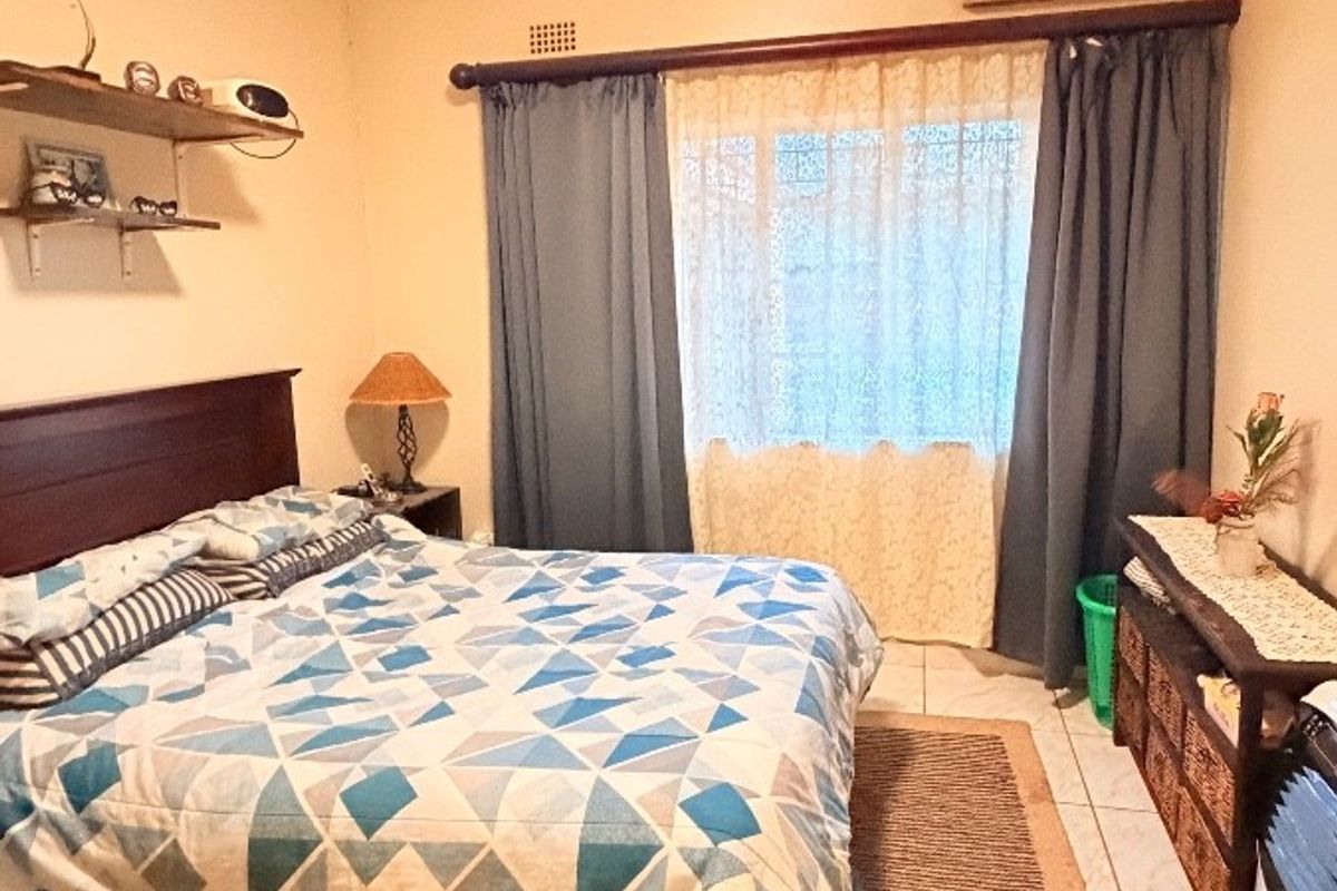 A bedroom featuring tiled flooring, a wall-mounted air conditioning unit, and a window with curtain rod.