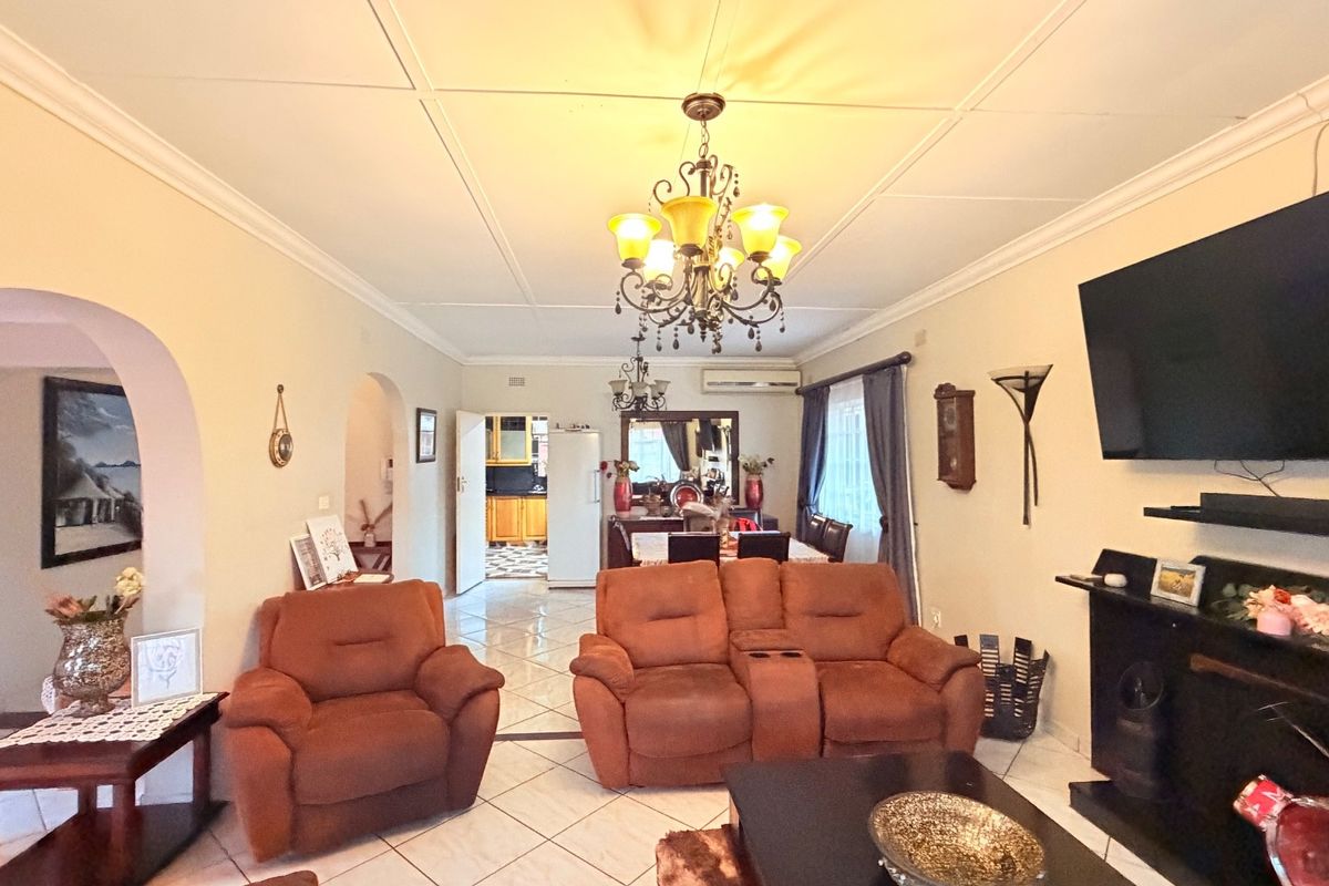 A spacious living room featuring tiled flooring, decorative ceiling panels, and an arched entryway leading to the kitchen area.