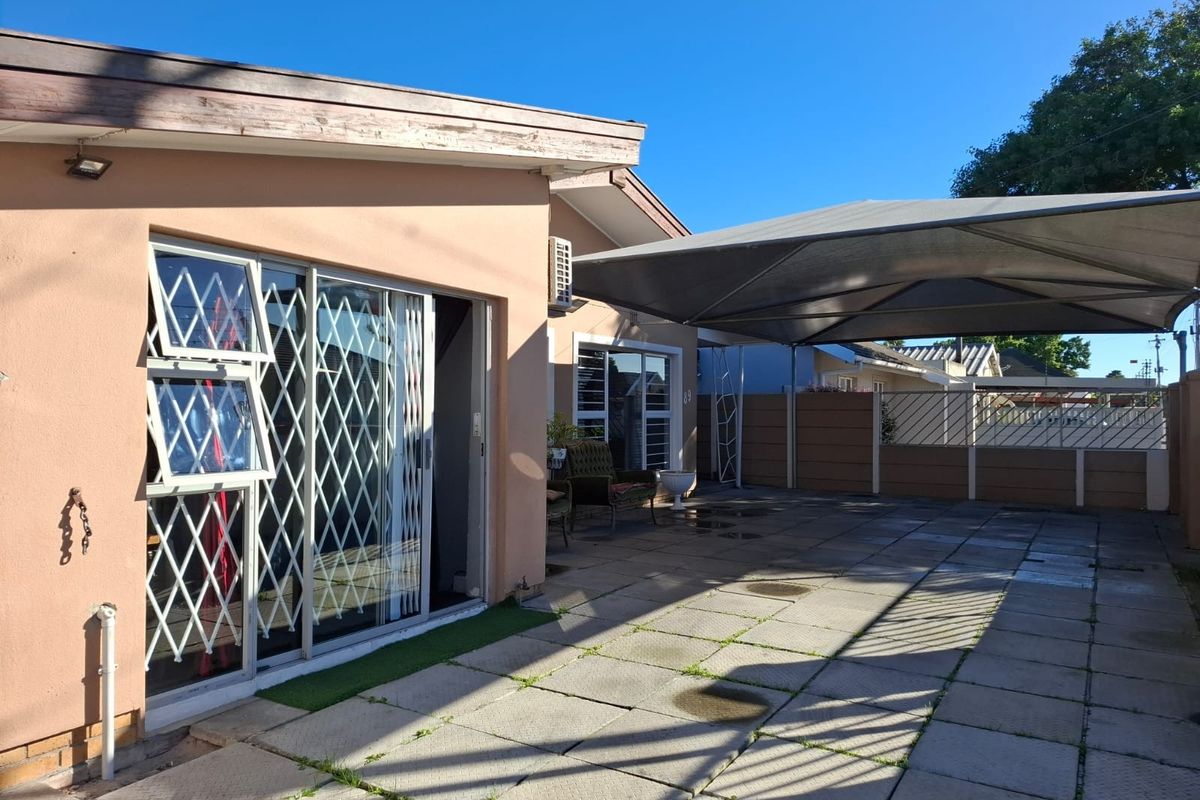 Rear exterior view featuring a paved patio area with a shade sail, sliding glass doors with security gates, and perimeter walling.
