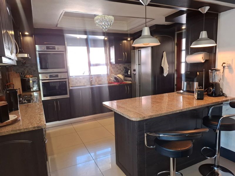 A well-appointed kitchen featuring dark cabinetry, granite countertops, a central breakfast island, and built-in double ovens with a gas hob.