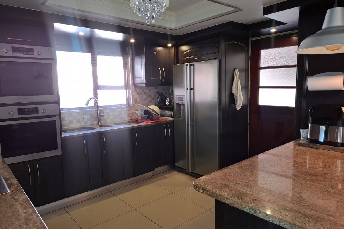 A well-appointed kitchen featuring dark cabinetry, granite countertops, a built-in double oven, and a central island with a breakfast bar.