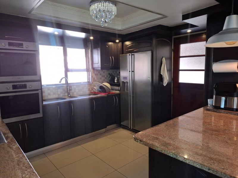 A well-appointed kitchen featuring dark cabinetry, granite countertops, a built-in double oven, and a central island with a breakfast bar.