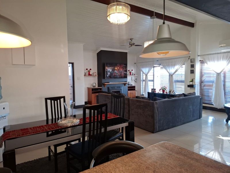 An open-plan living and dining area featuring high vaulted ceilings, tiled flooring, and a central fireplace with a built-in television mount.