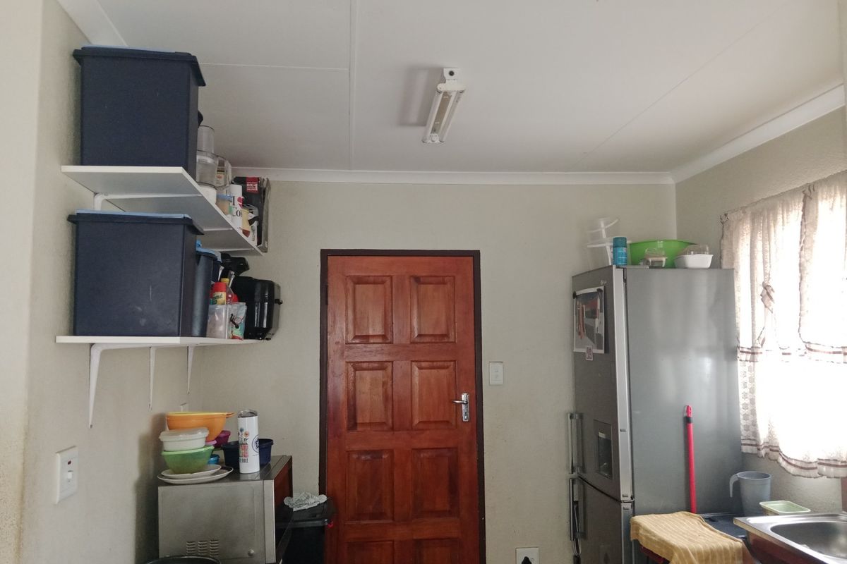 A functional kitchen area featuring wall-mounted shelving, a solid timber door, and a stainless steel sink unit.