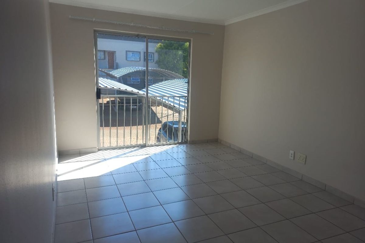 A bright, empty living room featuring neutral tiled flooring and a sliding glass door that opens to a balcony area.
