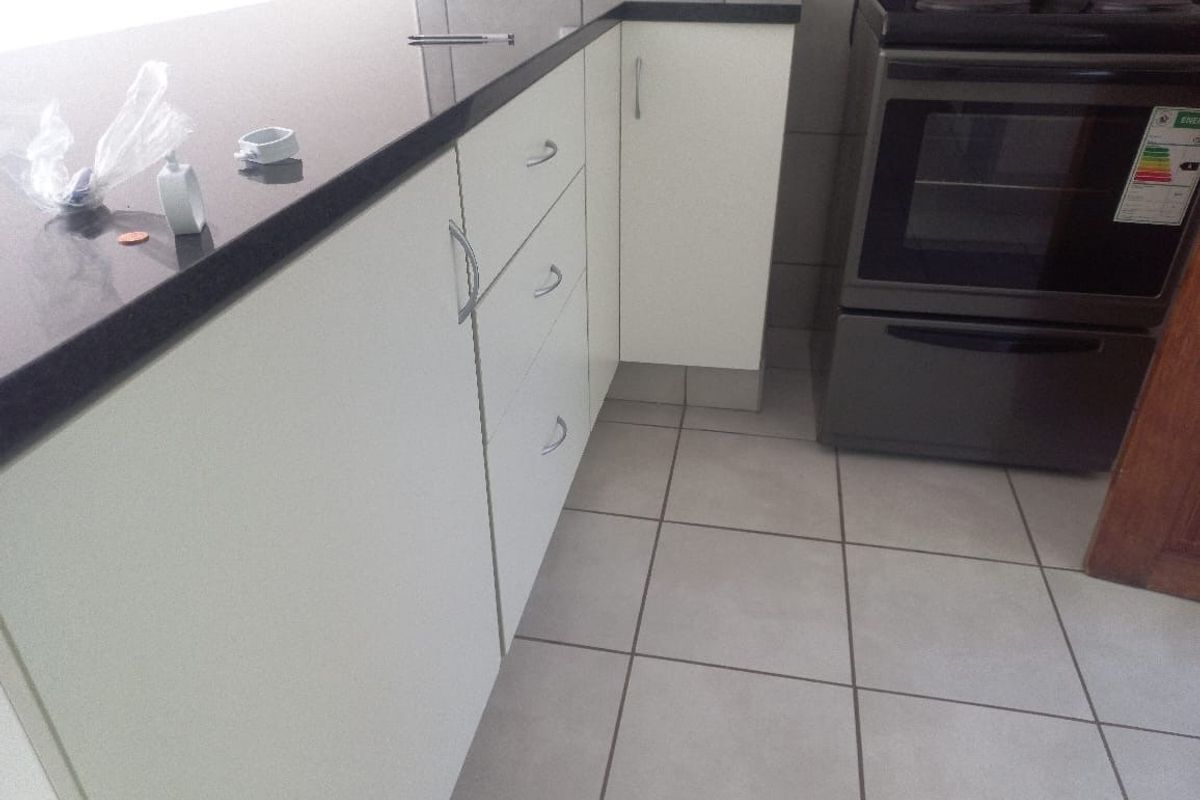 A functional kitchen area featuring white cabinetry, dark countertops, and tiled flooring, equipped with a built-in oven and stove.